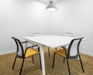 Minimalistisch vergaderruimte met een witte tafel, vier moderne stoelen en een industriële hanglamp.