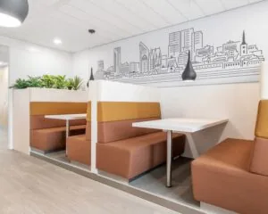Moderne kantoorzitplekken met oranje en bruine bankjes, een witte tafel en een muurtekening van de skyline van Den Haag.