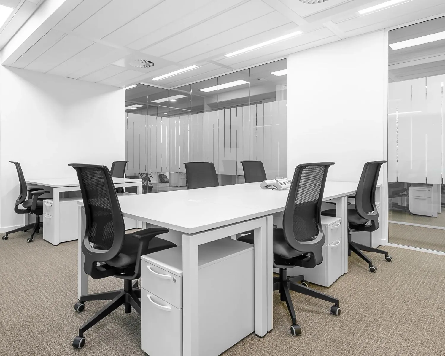 Moderne, minimalistische kantooruimte met witte bureaus, zwarte bureaustoelen en glazen scheidingswanden.