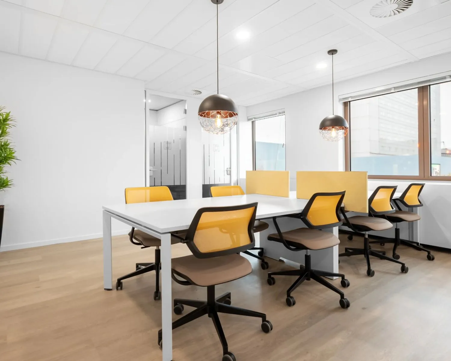 Moderne kantoorruimte met zes bureaustoelen, witte tafels en gele scheidingspanelen bij raam met veel daglicht.