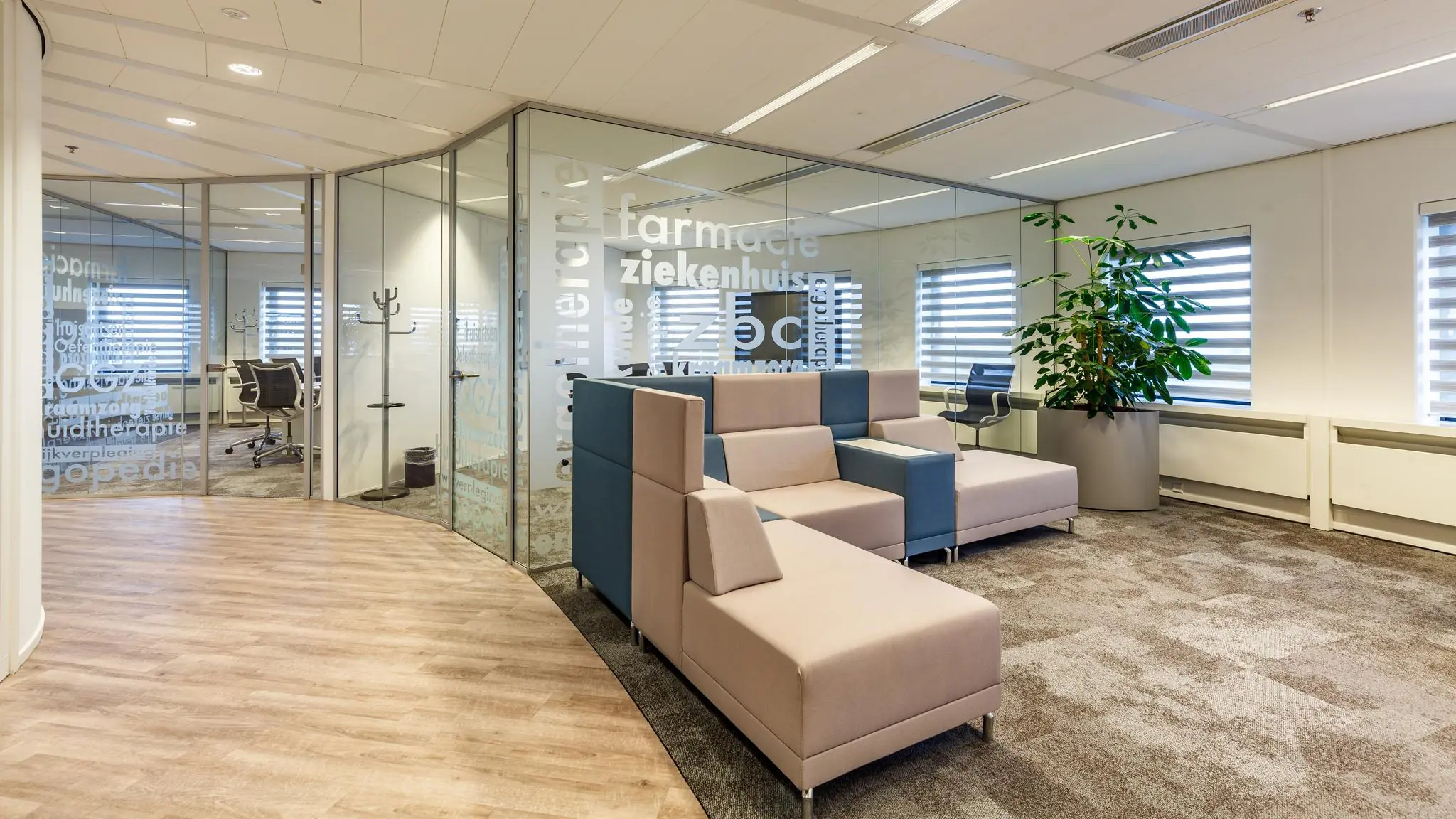 Moderne wachtruimte in een kantoorpand aan de Euclideslaan met glazen wanden, beige-blauwe zitbanken en een grote kamerplant.