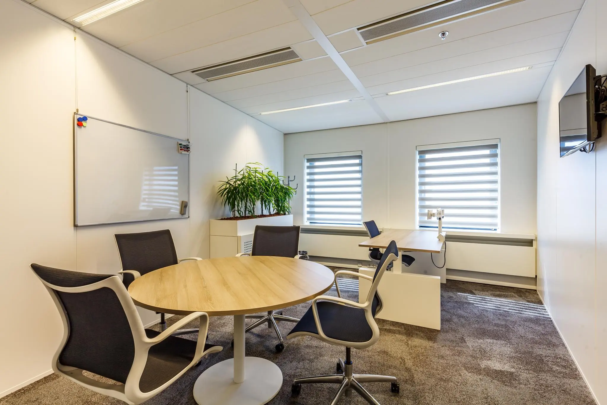 Modern ingericht kantoor aan de Euclideslaan met ronde vergadertafel, bureaus, whiteboard en grote ramen met zonwering.
