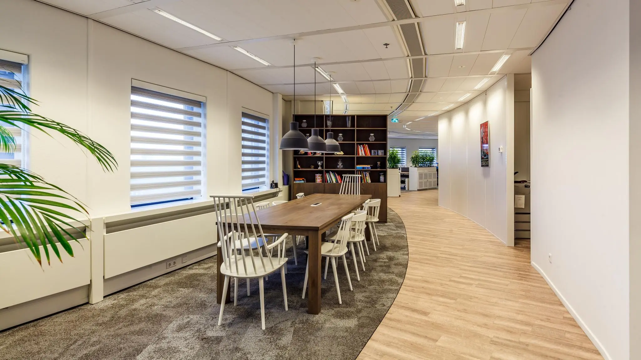 Moderne vergaderruimte aan de Euclideslaan met houten tafel, witte stoelen en open boekenkast in een kantooromgeving.
