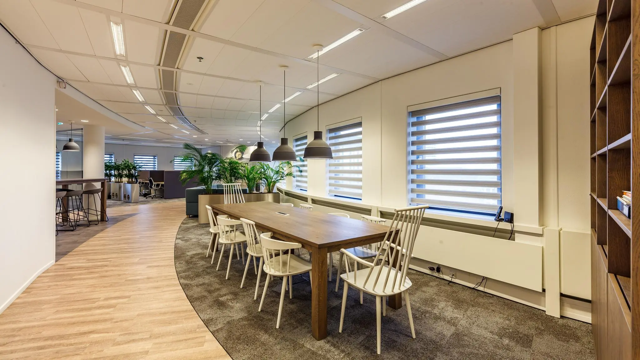 Moderne kantoorruimte aan de Euclideslaan met een lange houten vergadertafel, witte stoelen en hanglampen bij grote ramen met jaloezieën.