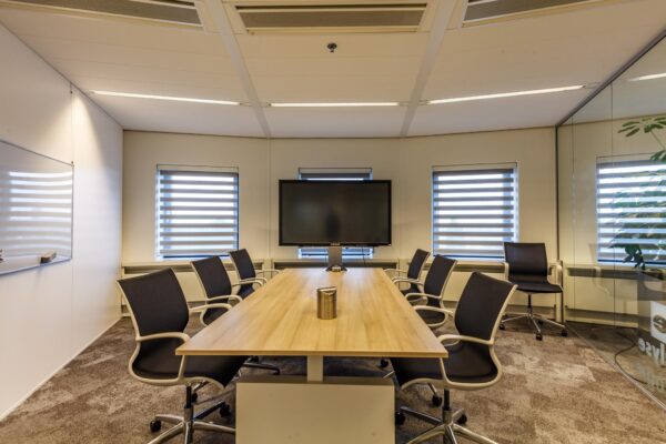 Moderne vergaderruimte aan de Euclideslaan met een lange houten tafel, acht stoelen, groot presentatiescherm en strakke inrichting.