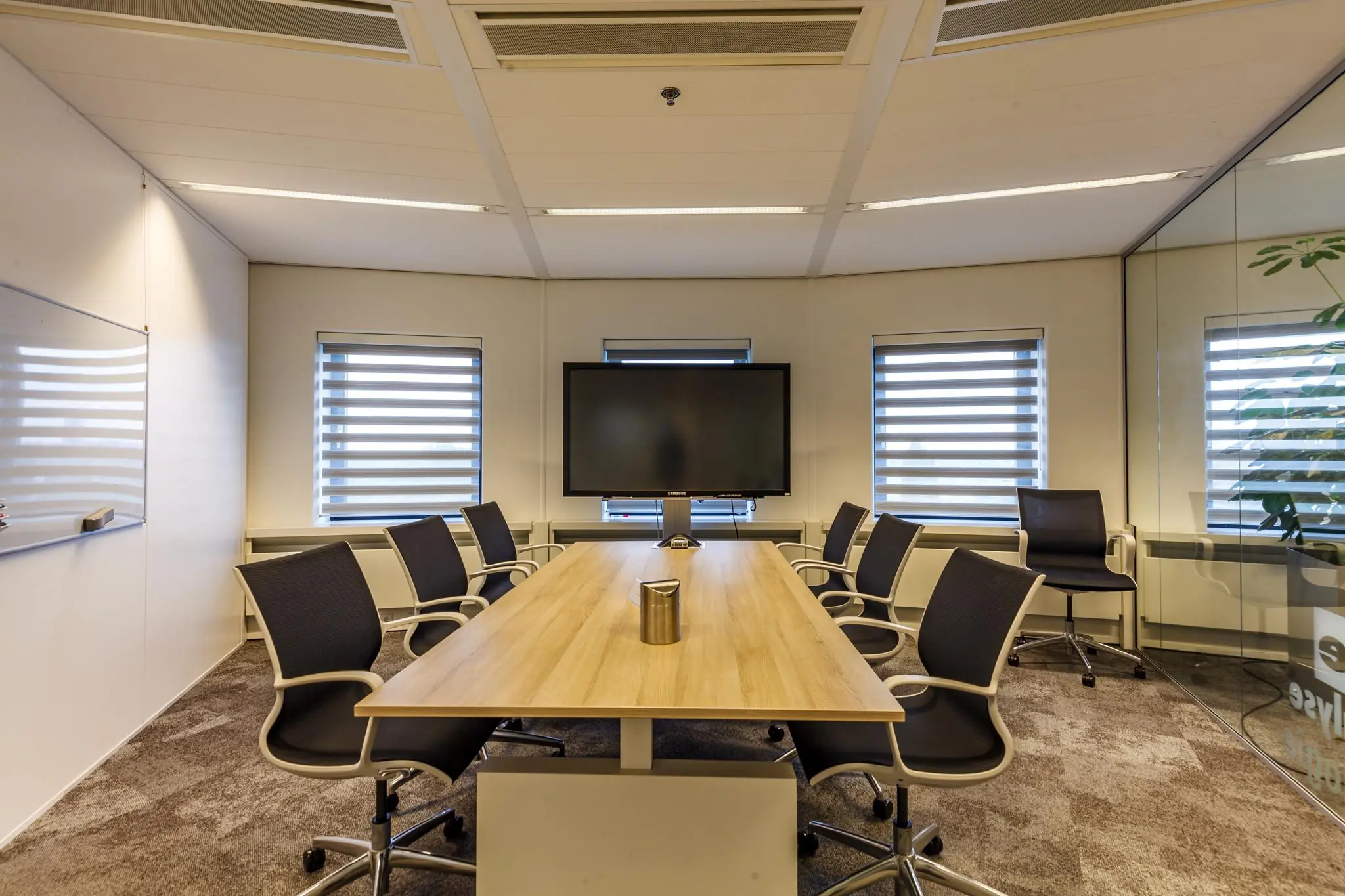 Moderne vergaderruimte aan de Euclideslaan met een lange houten tafel, acht stoelen, groot presentatiescherm en strakke inrichting.