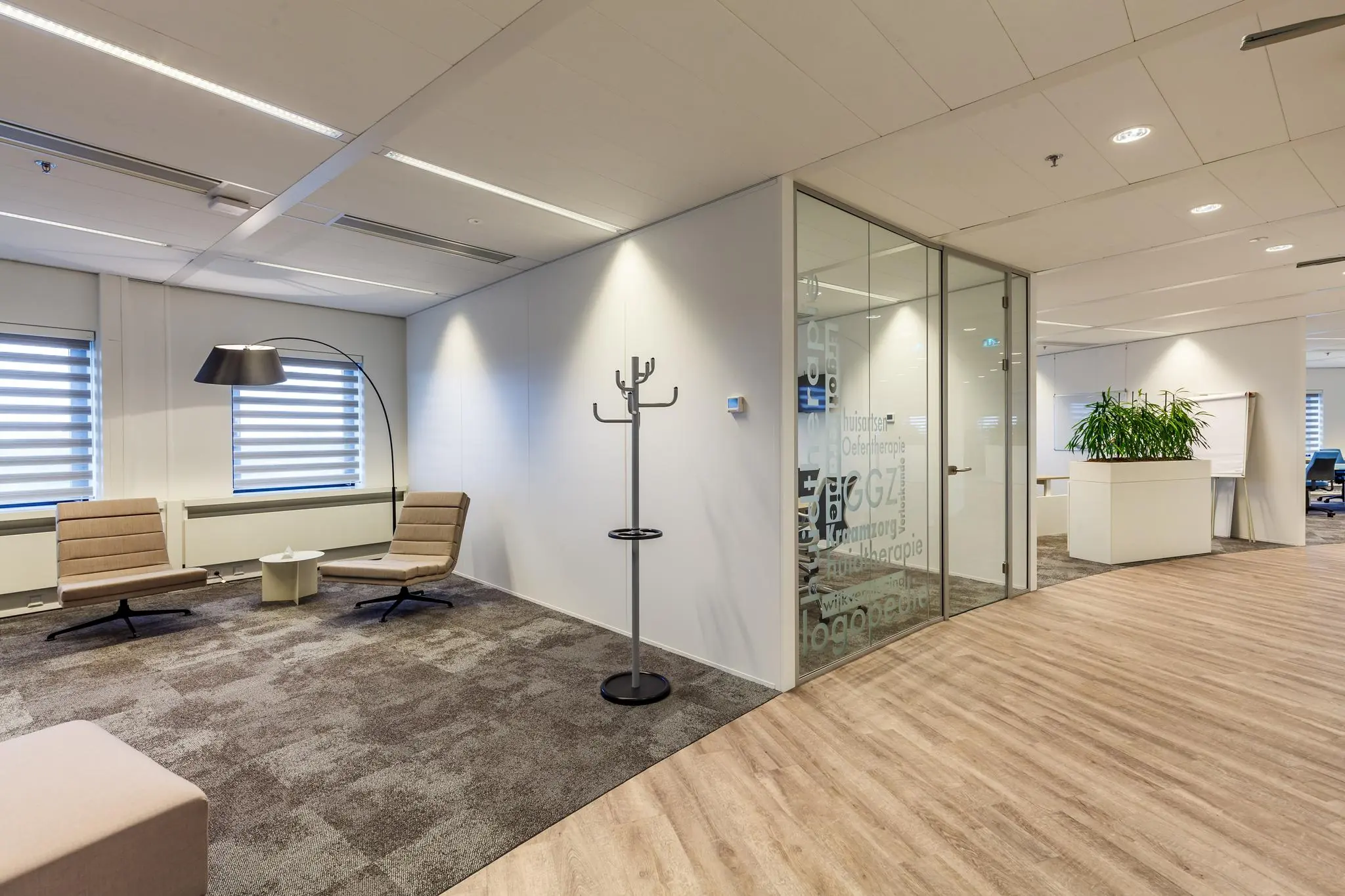 Moderne wachtruimte aan de Euclideslaan met twee stoelen, een staande lamp en glazen kantoorruimte op de achtergrond.