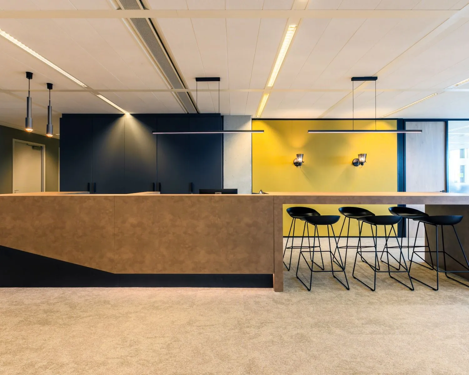 Moderne receptiebalie met zwarte barkrukken en een opvallende gele achterwand in een strak ingericht kantoorinterieur.