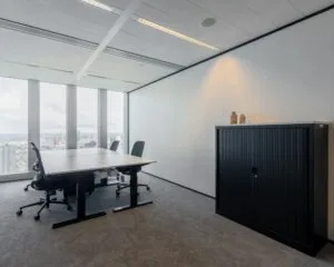 Moderne vergaderruimte met vier bureaustoelen, een tafel en een zwart opbergmeubel, met uitzicht op de stad door grote ramen.