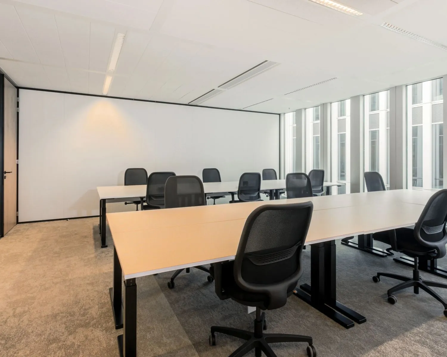 Moderne, lichte kantoorruimte met meerdere bureaus en zwarte bureaustoelen.