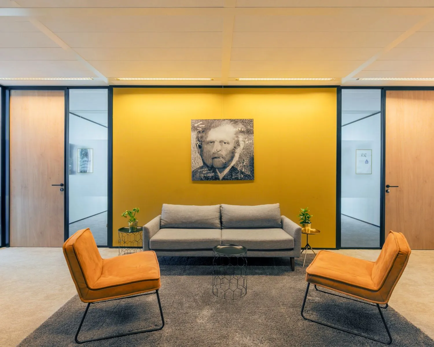 Moderne wachtruimte met gele accentmuur, grijze bank, oranje stoelen en een kunstwerk van Vincent van Gogh aan de muur.
