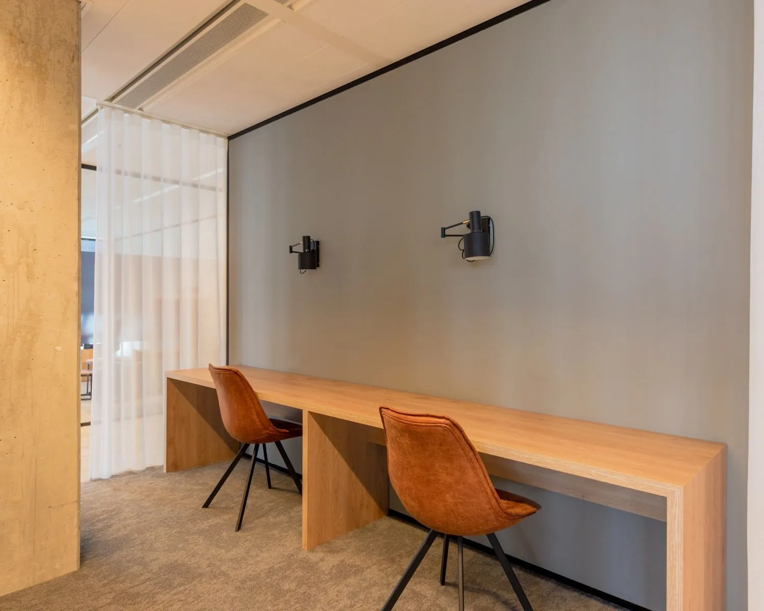 Stijlvolle werkplek met een lange houten tafel, twee bruine stoelen en wandlampen tegen een grijze muur.