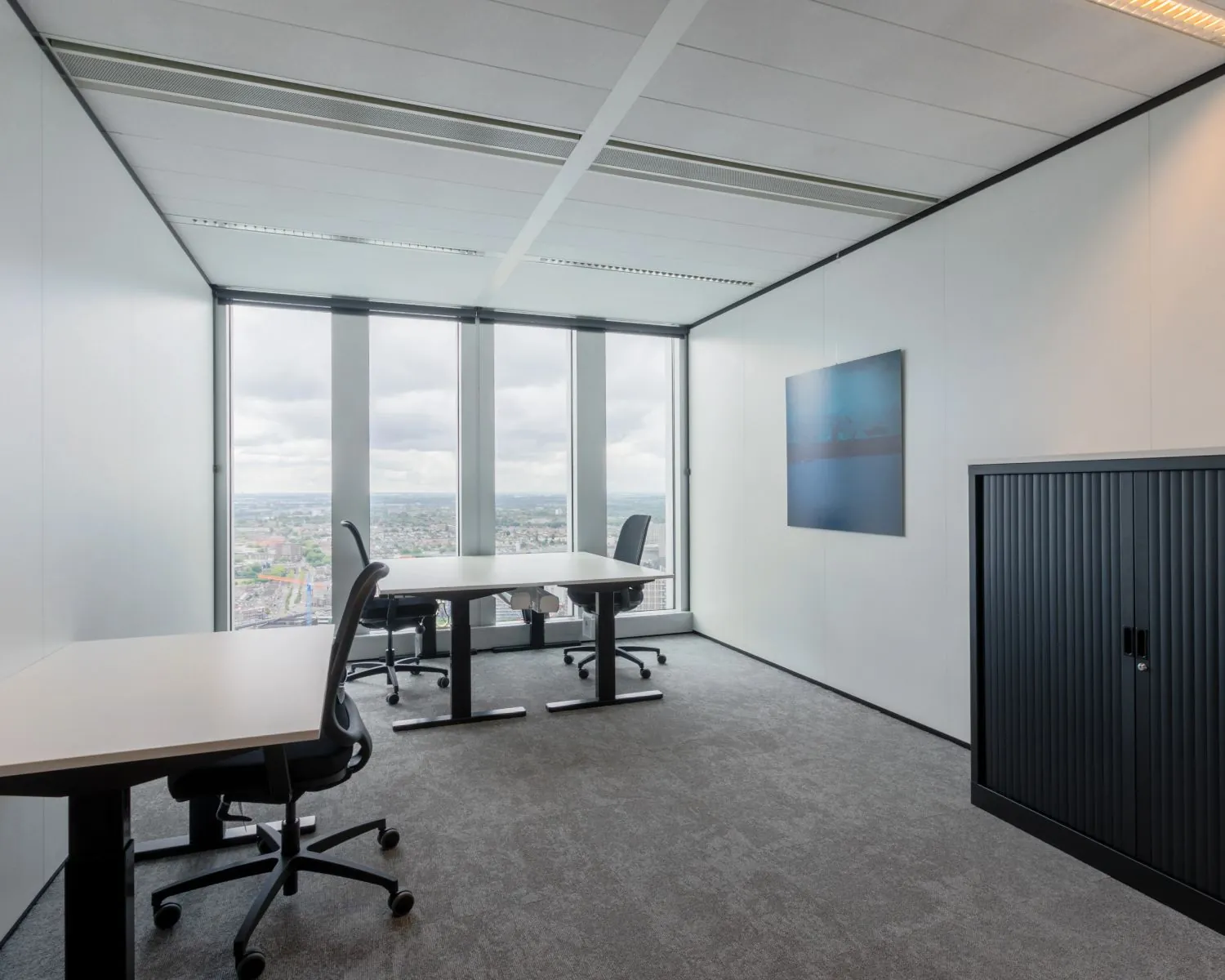 Moderne, lichte kantoorruimte met vier bureaus, ergonomische stoelen en grote ramen met uitzicht over de stad.