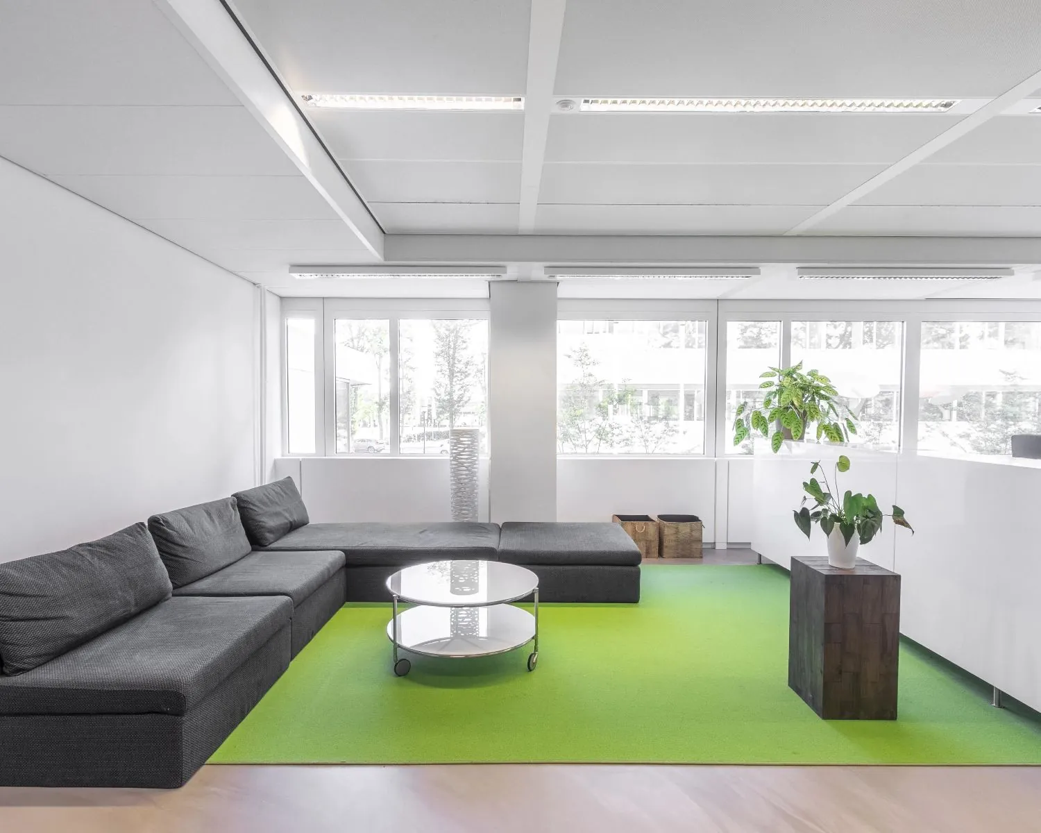 Moderne kantoorruimte in Whitepark Delft met een grijze loungebank, glazen salontafel en groene vloerbedekking.