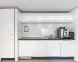 Moderne pantry met witte kasten, zwart aanrechtblad en een luxe koffiemachine in een kantoorruimte aan de Poortweg 4 in Delft.