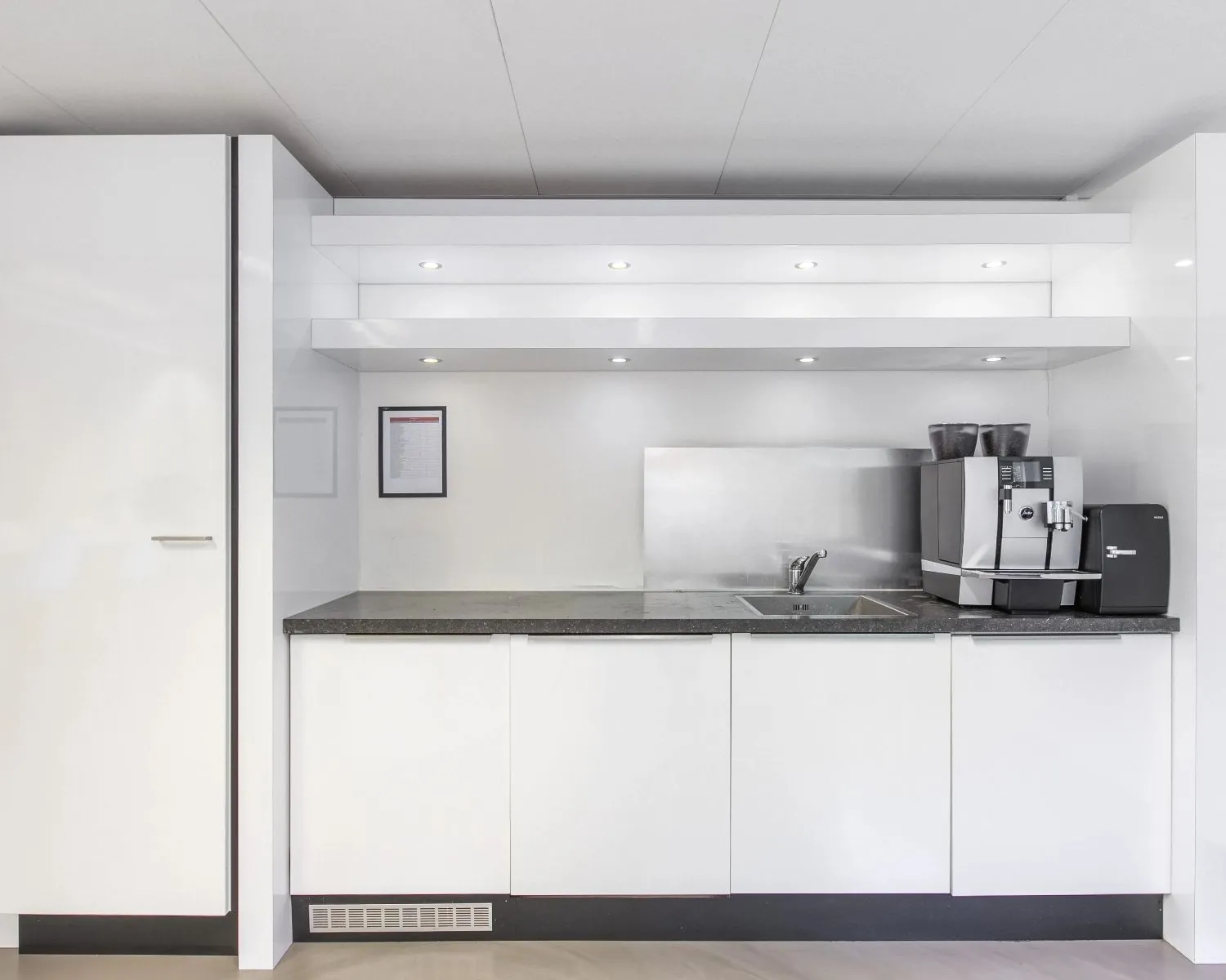 Moderne pantry met witte kasten, zwart aanrechtblad en een luxe koffiemachine in een kantoorruimte aan de Poortweg 4 in Delft.