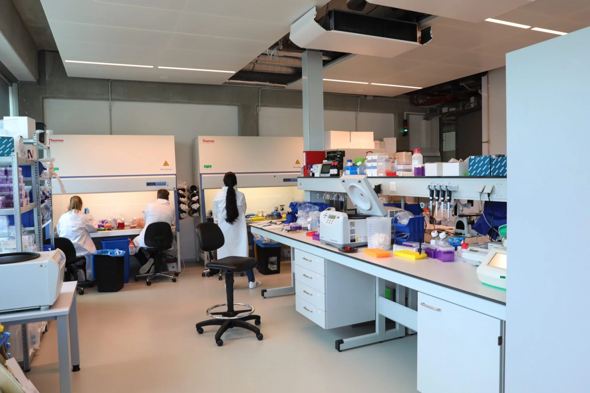 Wetenschappers in witte jassen werken in een modern laboratorium met laboratoriumapparatuur en veiligheidskasten van Thermo.