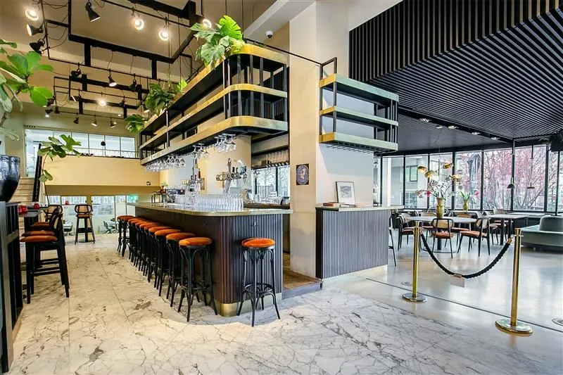 Moderne, stijlvol ingerichte bar met marmeren vloer, hoge barkrukken en veel natuurlijke lichtinval.