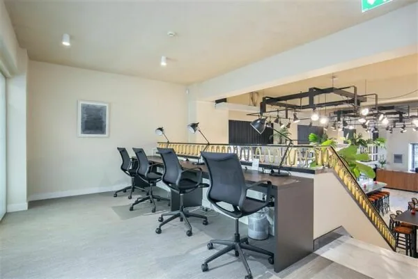 Moderne kantoorruimte met vier bureaus, bureaustoelen en bureaulampen op een open verdieping met zicht op benedenverdieping.
