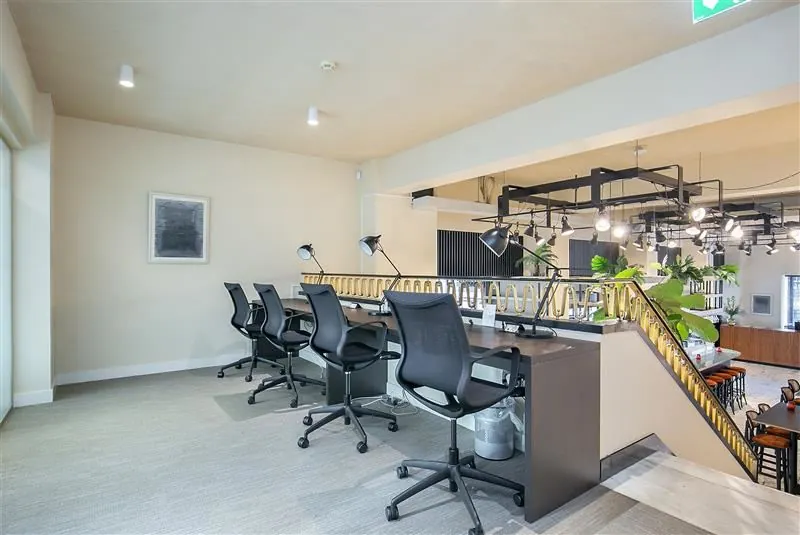 Moderne kantoorruimte met vier bureaus, bureaustoelen en bureaulampen op een open verdieping met zicht op benedenverdieping.