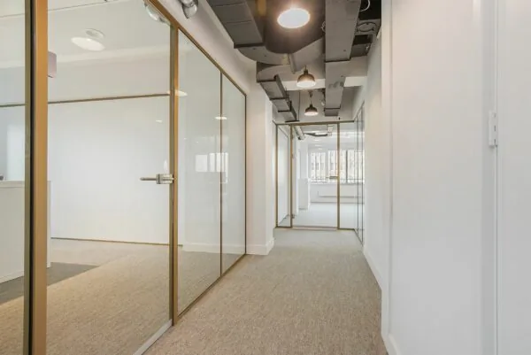 Modern kantoorinterieur met glazen wanden, beige vloerbedekking en industriële plafonddetails.