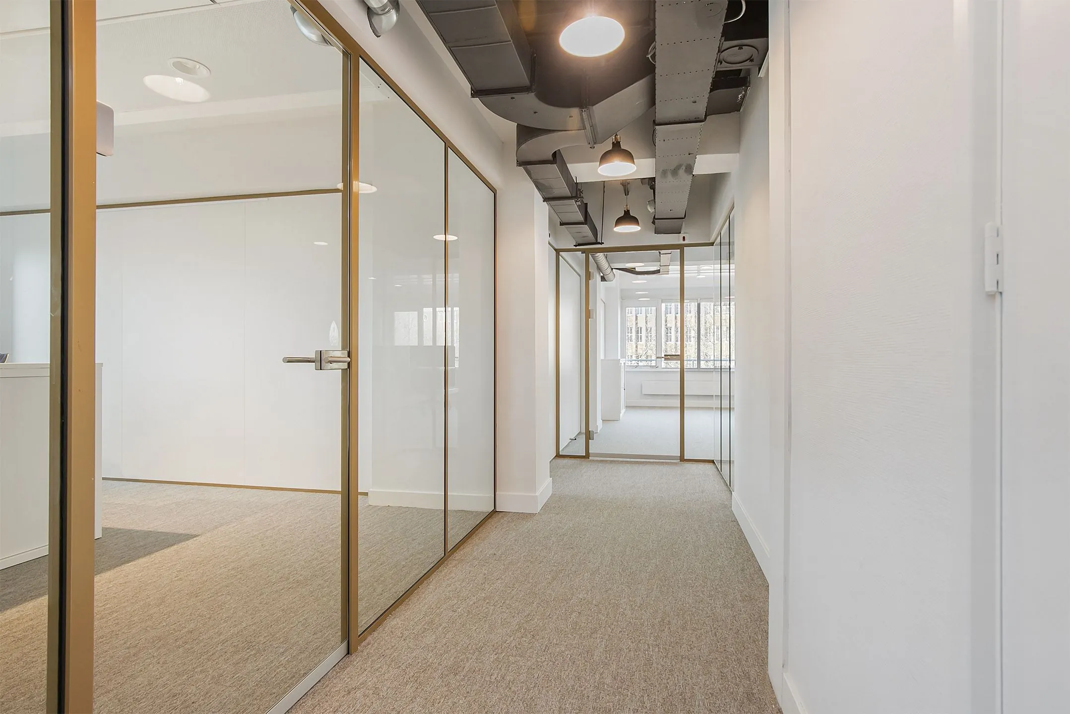 Modern kantoorinterieur met glazen wanden, beige vloerbedekking en industriële plafonddetails.