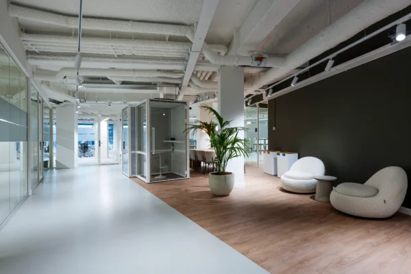 Een modern kantoorinterieur met een glazen spreekkamer, kamerplant, en comfortabele stoelen.