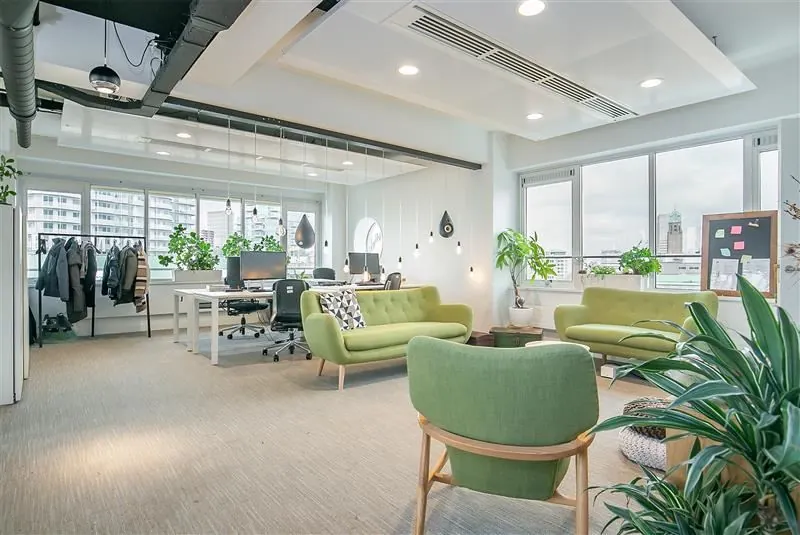 Modern kantoor met een open indeling, groene zithoek en veel natuurlijk licht.