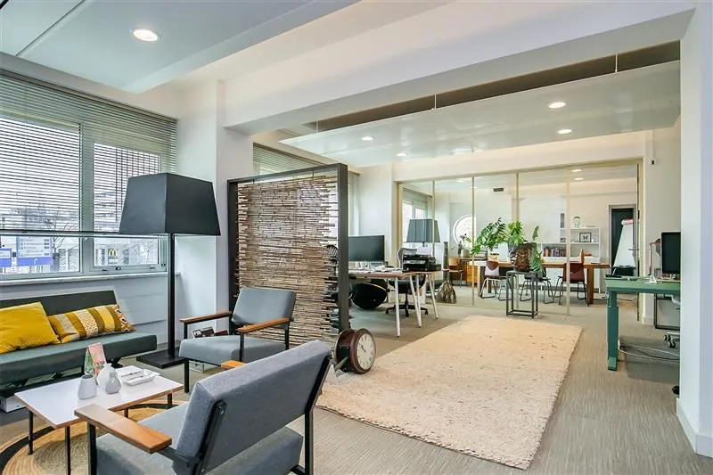 Modern ingerichte kantoorruimte met zithoek, werkplekken en veel natuurlijk lichtinval.
