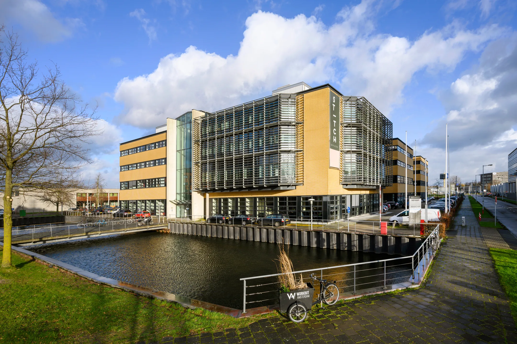 Modern kantoorgebouw met grote ramen langs een waterpartij en een fiets ernaast geparkeerd.