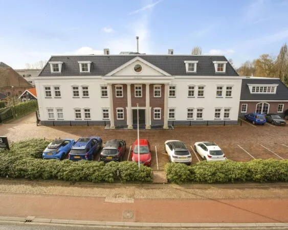 Vooraanzicht van een groot, klassiek kantoorgebouw genaamd 'Markanter', met geparkeerde auto’s op de oprijlaan.