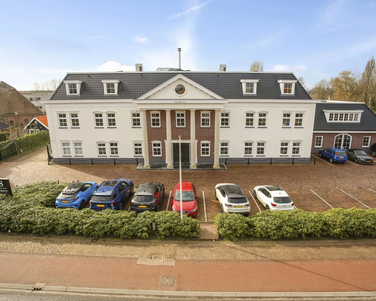 Vooraanzicht van een groot, klassiek kantoorgebouw genaamd 'Markanter', met geparkeerde auto’s op de oprijlaan.