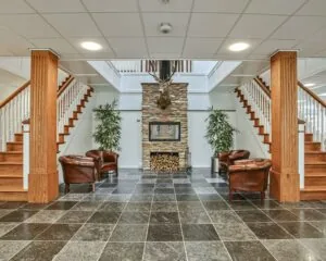 Ruime ontvangstruimte met een open haard, leren fauteuils, houten trap en een opgezette hertenkop aan de muur.