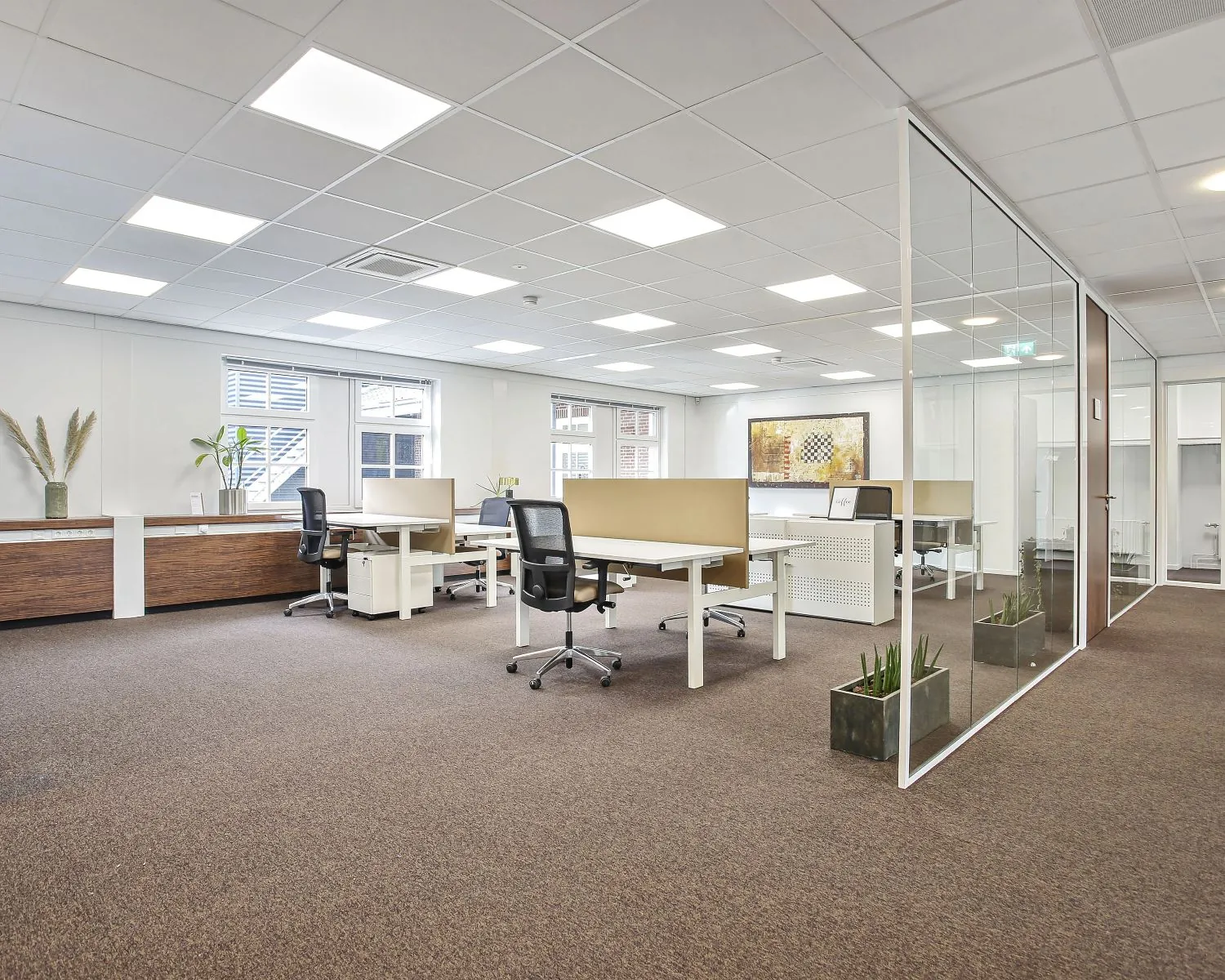 Moderne, lichte kantooruimte met meerdere bureaus, ergonomische stoelen en glazen scheidingswand.
