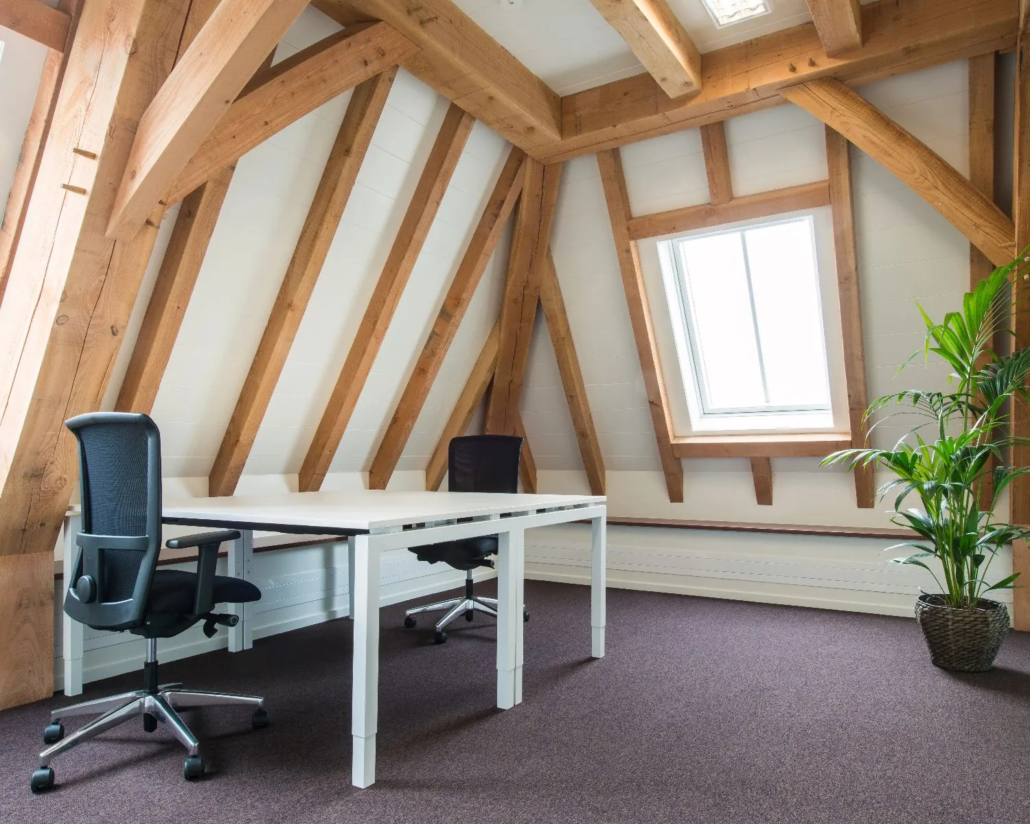 Modern kantoor met twee bureaustoelen onder een schuin dak met houten balken en een dakraam.