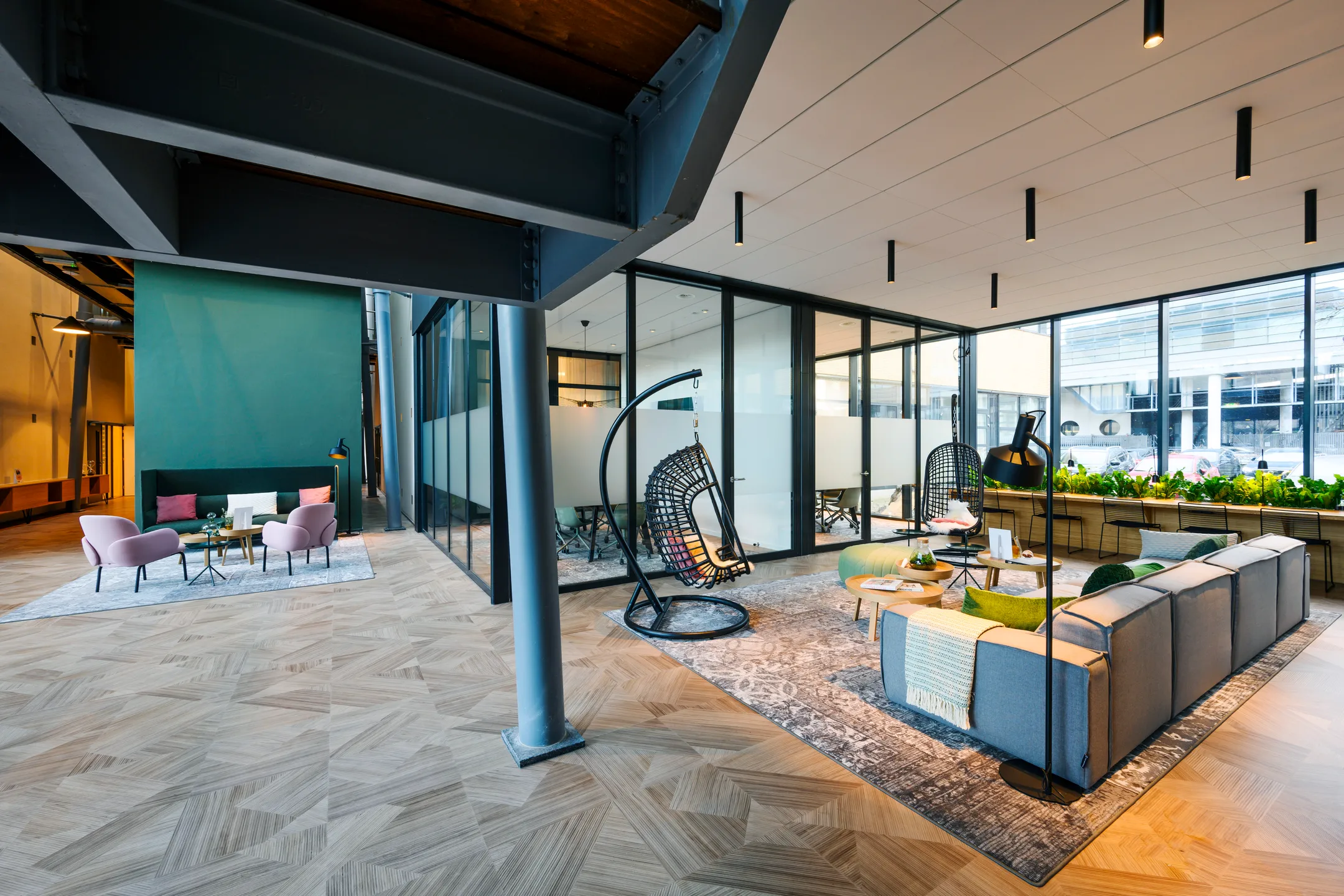 Een moderne kantoorruimte met glazen wanden, hangstoelen en een zithoek met groene en roze accenten.