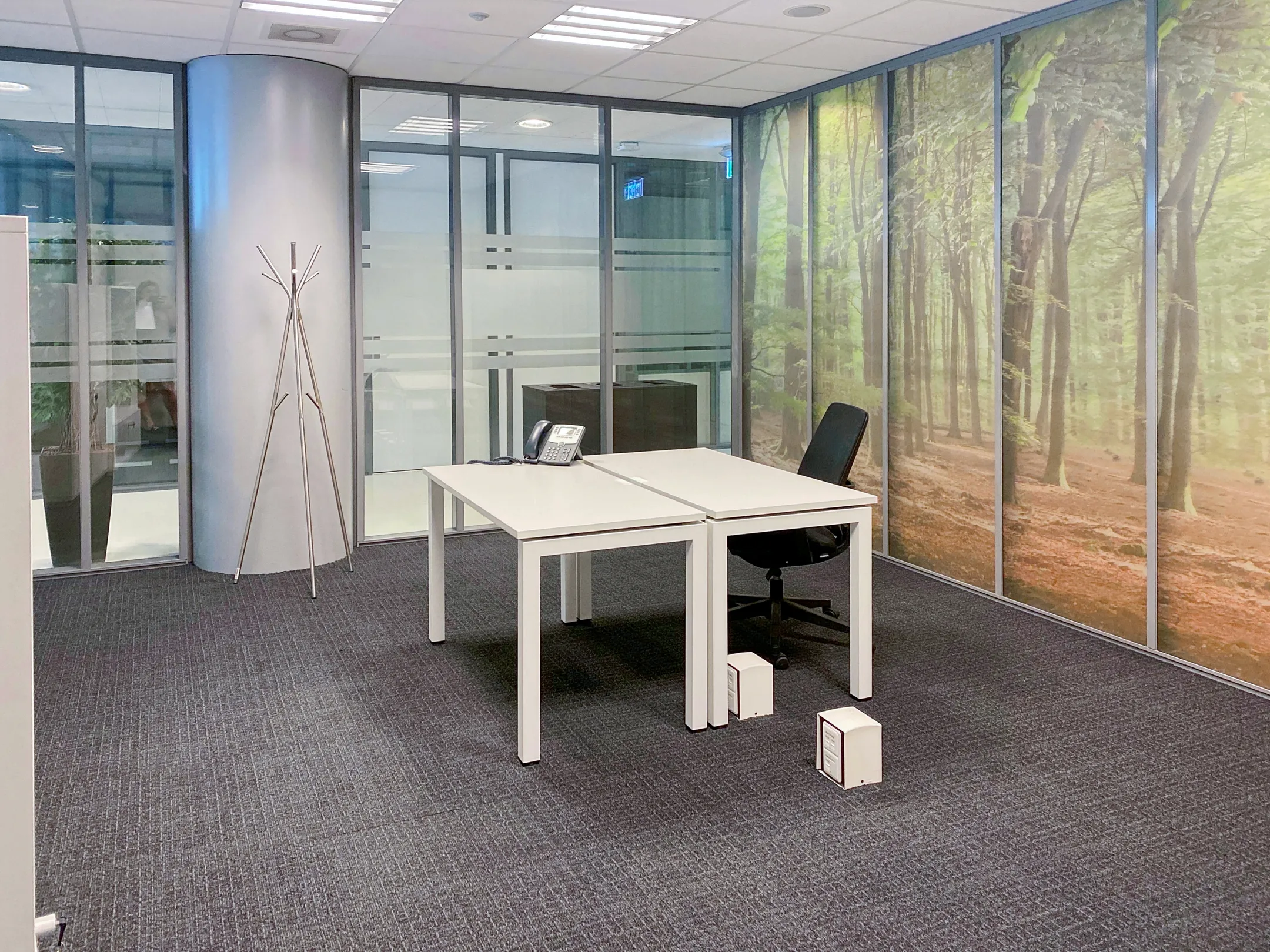 Een modern kantoor met een bureau, stoel, telefoon en een muurdecoratie van een boslandschap.