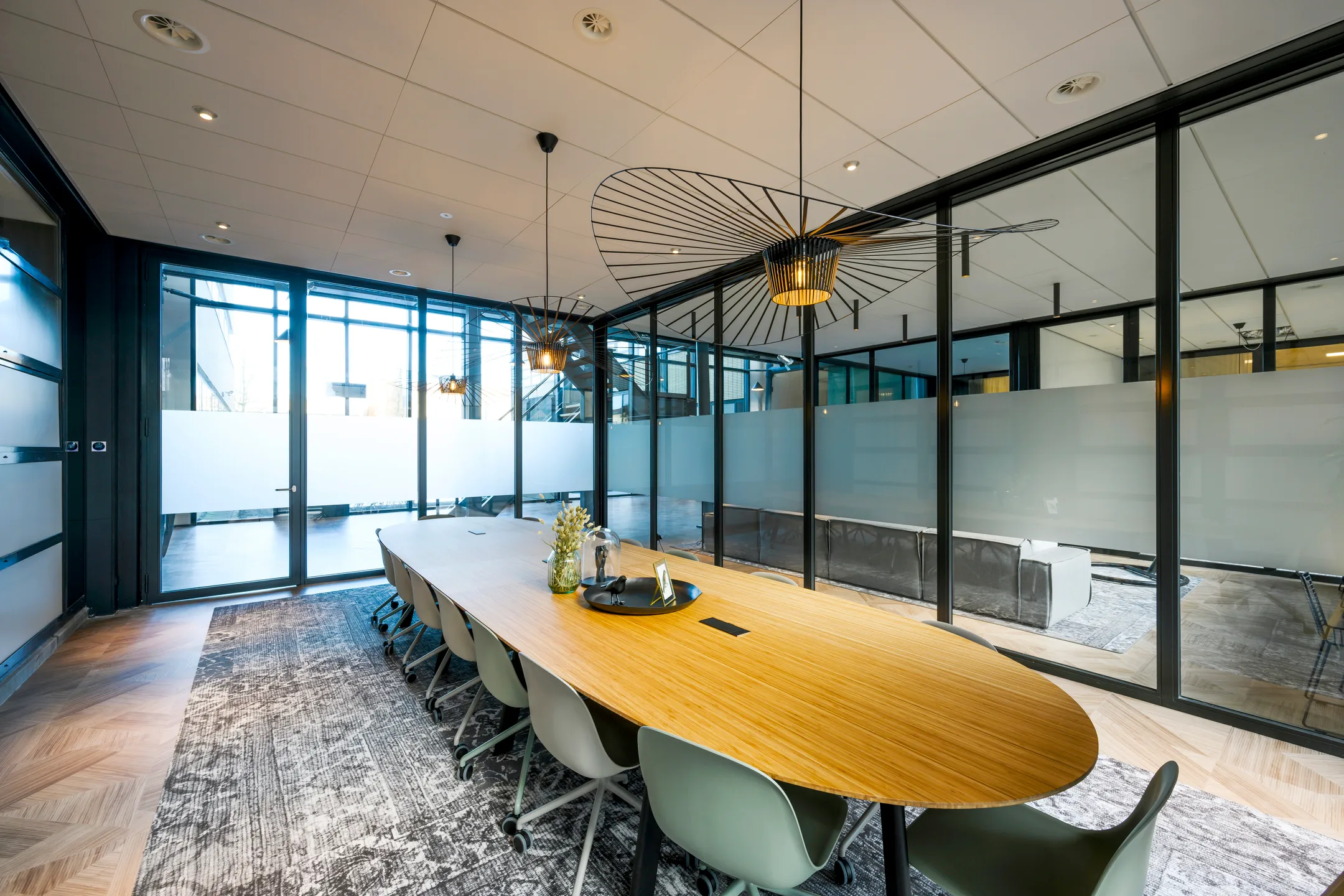 Een moderne vergaderruimte met een lange houten tafel, omringd door stoelen en voorzien van stijlvolle hanglampen.