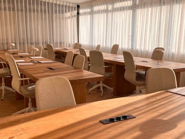 Lichte en moderne vergaderruimte met houten tafels, beige stoelen en bureaulampen in het zachte zonlicht.