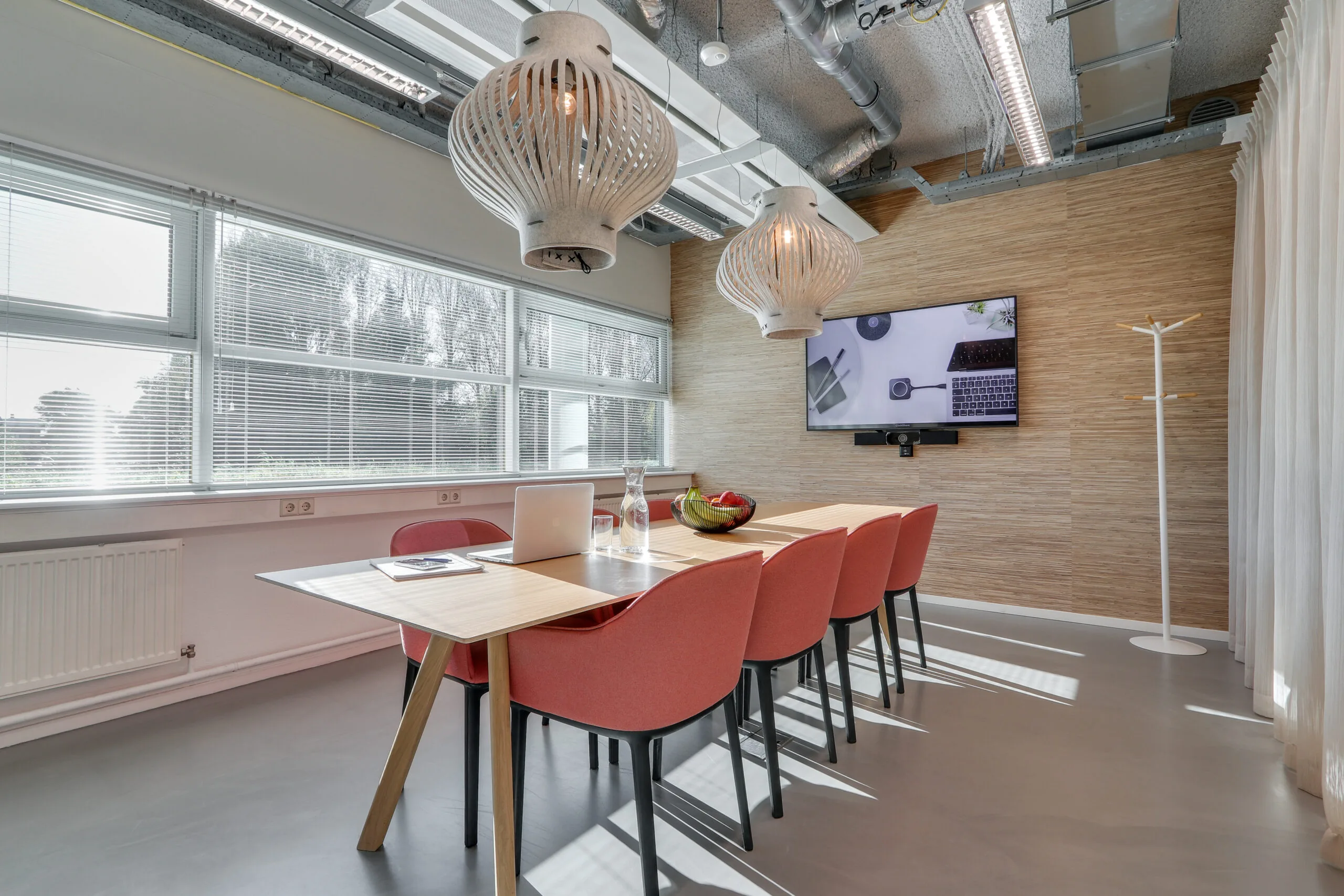 Moderne vergaderruimte in Amsterdam Zuidoost met houten tafel, rode stoelen, hanglampen en flatscreen aan de muur.