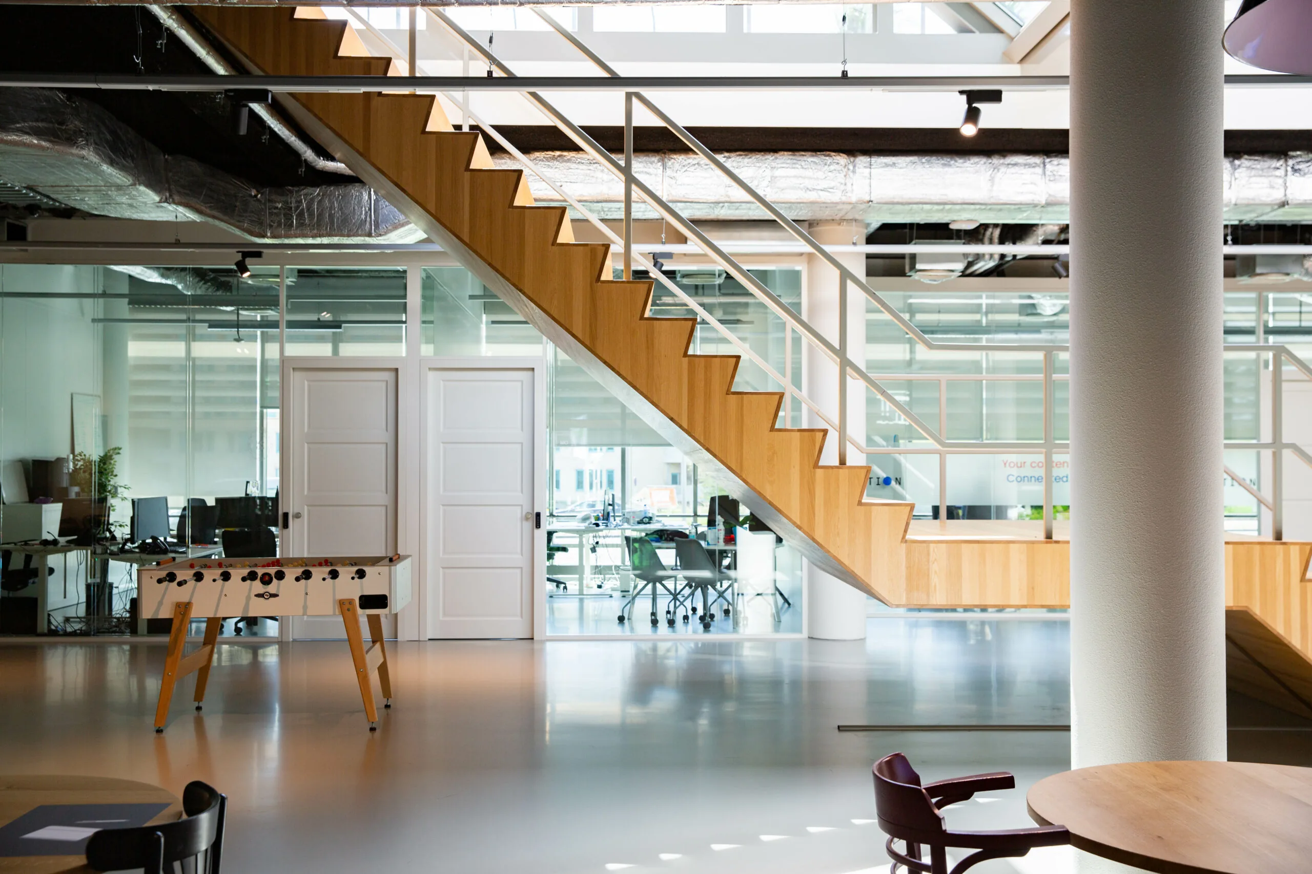 Moderne kantoorruimte in HNK Den Haag met een houten trap, glazen wanden en een tafelvoetbaltafel.