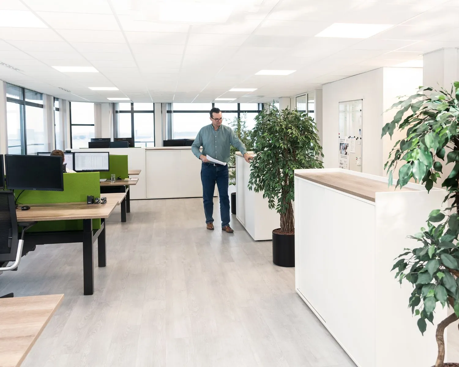 Moderne kantoorruimte aan de Pascallaan 60-78 in Lelystad met werkplekken, planten en een man die door het kantoor loopt.