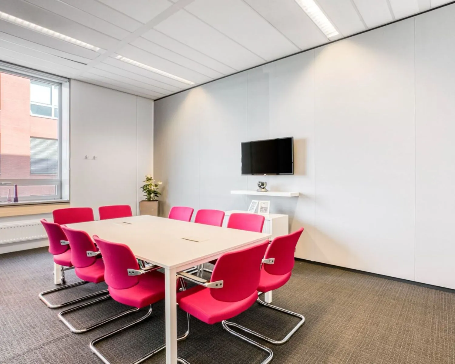 Moderne vergaderruimte met roze stoelen en witte tafel in kantoorruimte Flight Forum 40 in Eindhoven.