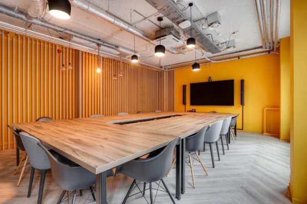 Moderne vergaderruimte in Rotterdam Centrum met U-vormige houten tafel, gele muren en een groot presentatiescherm.