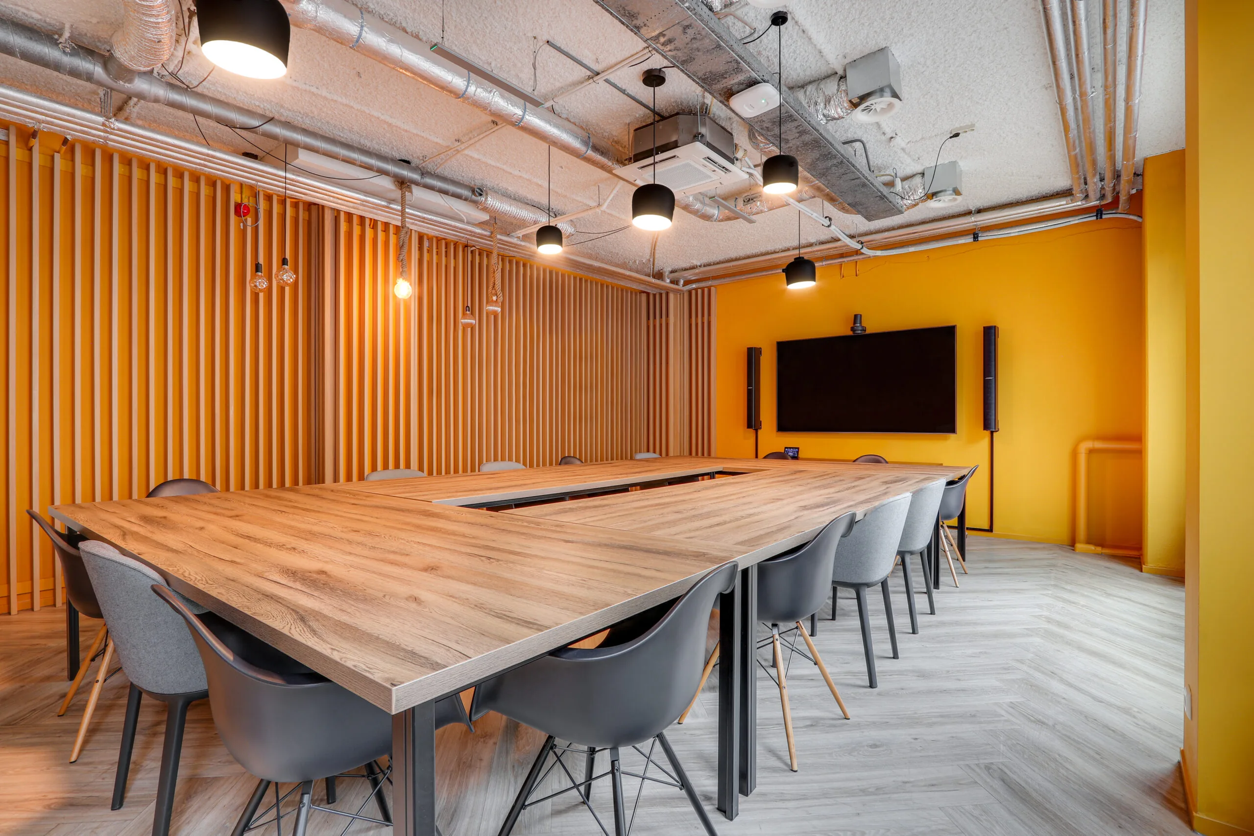 Moderne vergaderruimte in Rotterdam Centrum met U-vormige houten tafel, gele muren en een groot presentatiescherm.