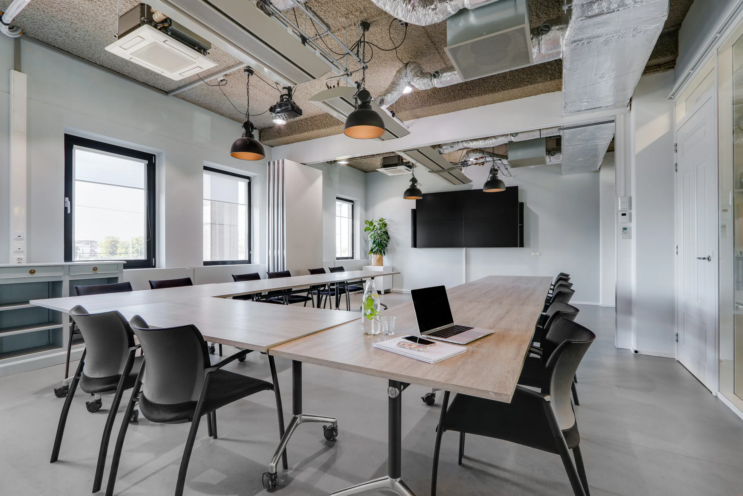 Moderne vergaderruimte op Utrecht Centraal met U-vormige opstelling, laptop, notitieboek en grote presentatieschermen.