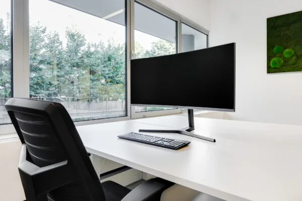 Een moderne co-working werkplek in Utrecht West met een groot beeldscherm, toetsenbord en bureaustoel bij een raam met uitzicht op groen.