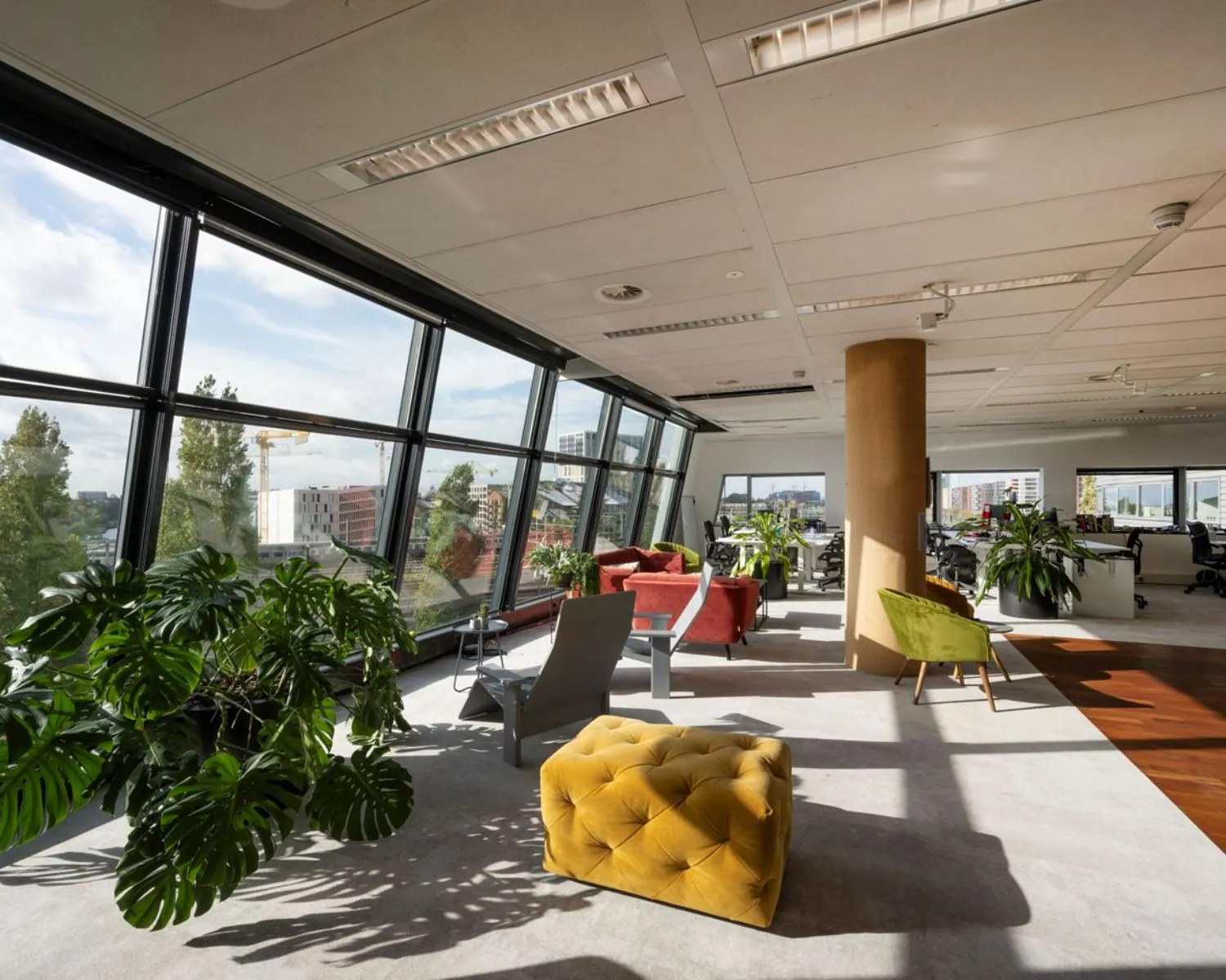Moderne kantoorruimte met grote raampartijen, kleurrijke zitplekken en veel natuurlijk licht aan het Rietlandpark in Amsterdam.