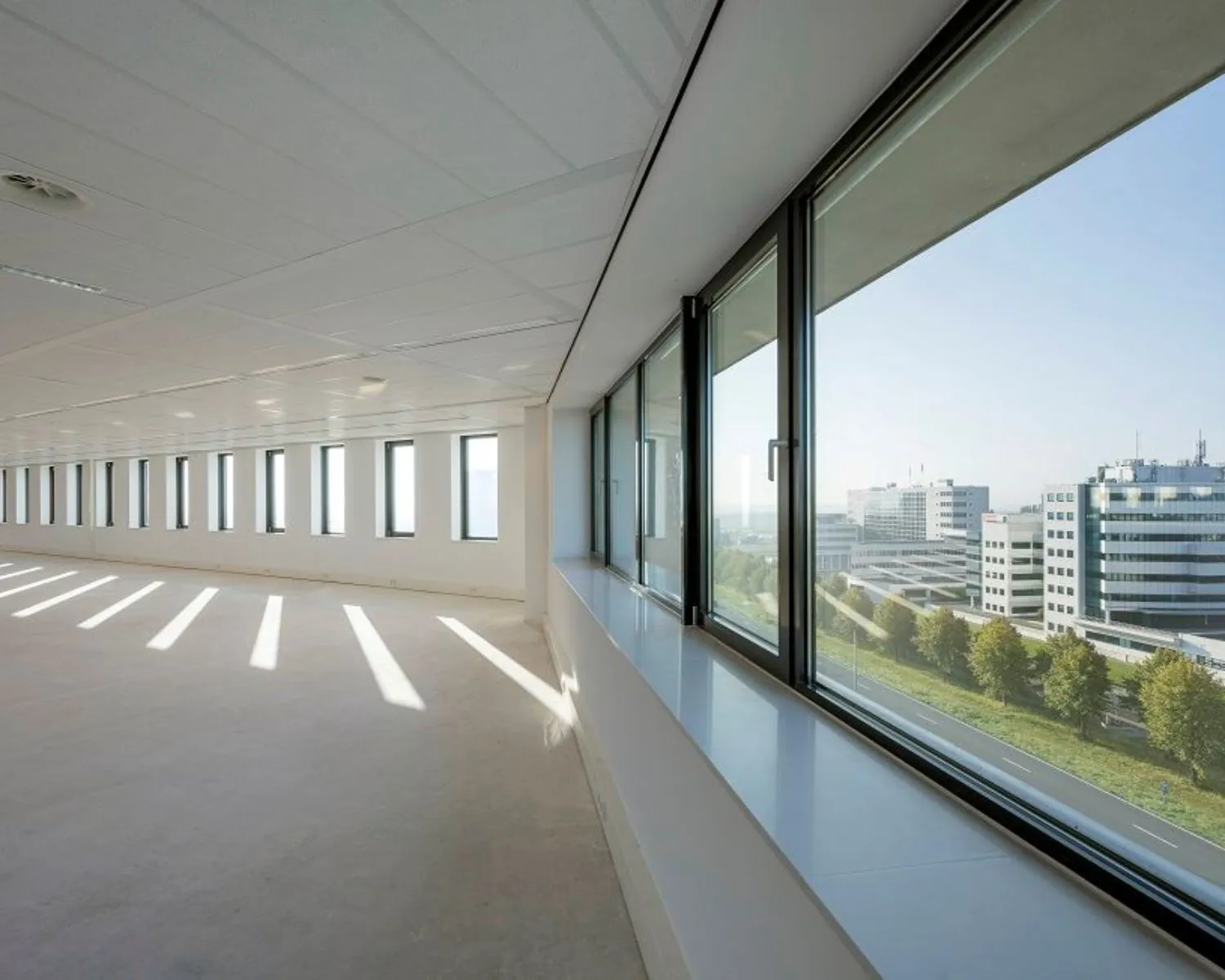 Lichte, lege kantoorruimte met grote ramen en uitzicht op kantoorgebouwen aan de Bloemlaan 2 in Hoofddorp.