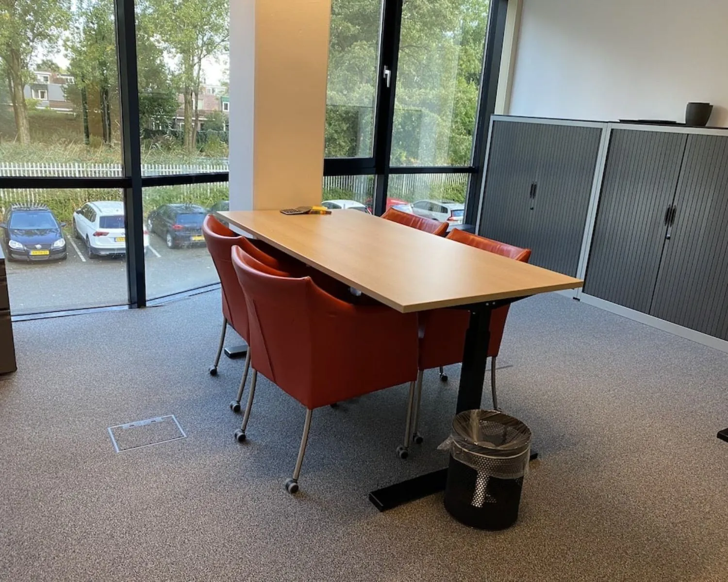 Moderne kantoorruimte in Elisabethhof Leiderdorp met vergadertafel, rode stoelen en uitzicht op parkeerplaats.